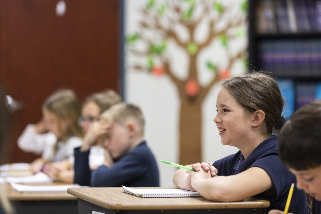 Elementary student sitting with a notebook out and hands clasped on her desk.